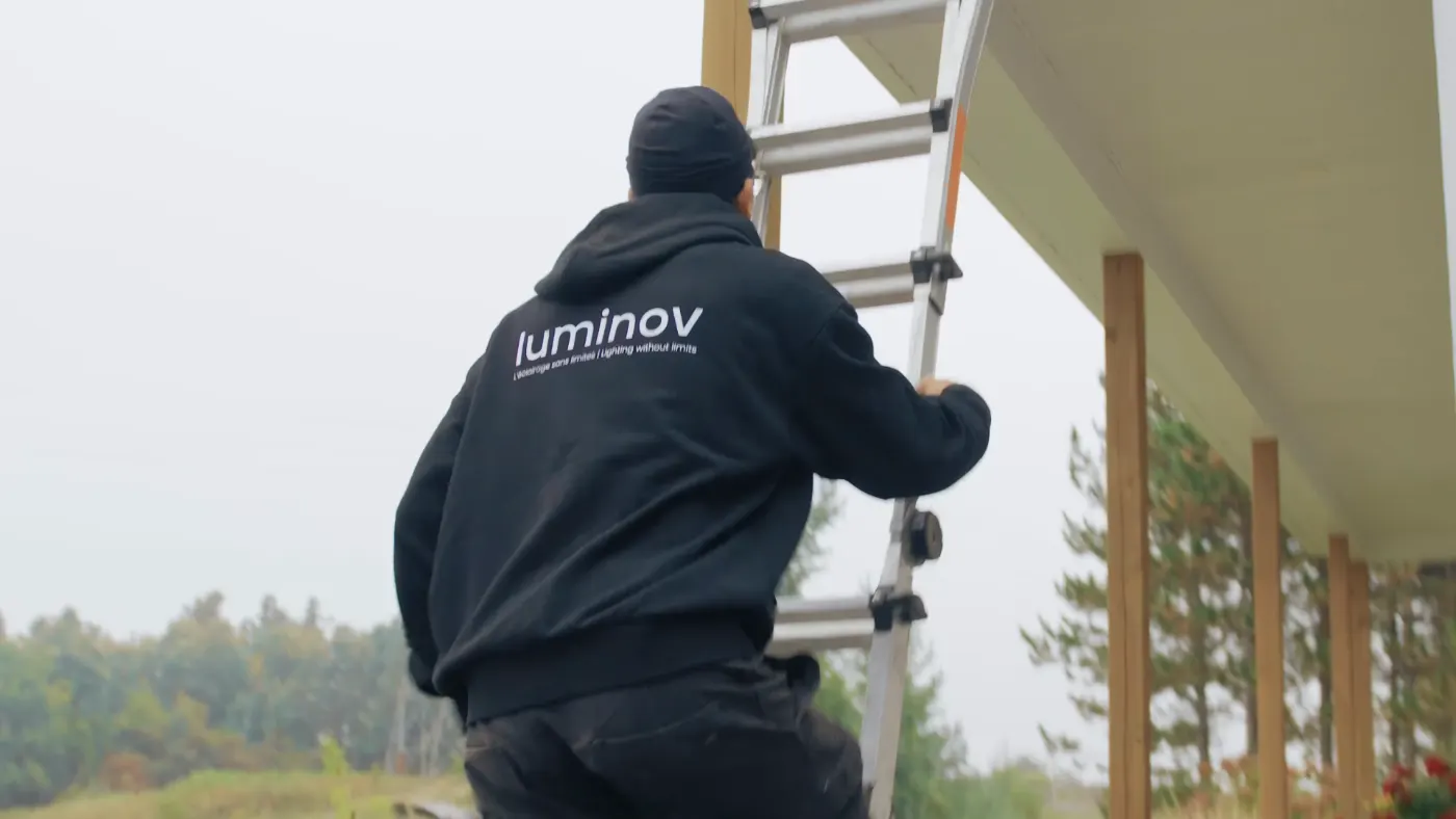 Installateur Luminov, logo sur le dos du hoodie, qui monte dans une échelle